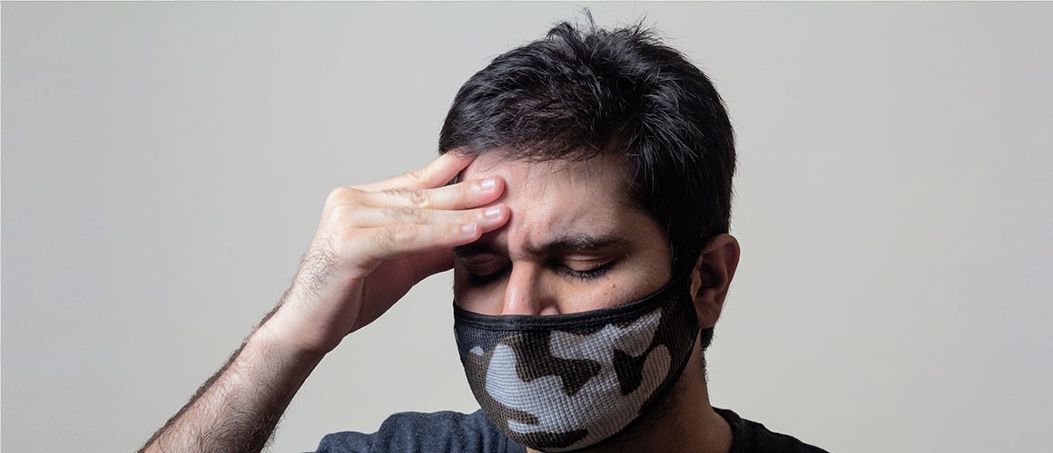 Picture of a man wearing a mask, touching his head.